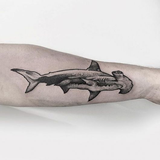 Tatuagem realista de um tubarão martelo nadando feita no antebraço. 