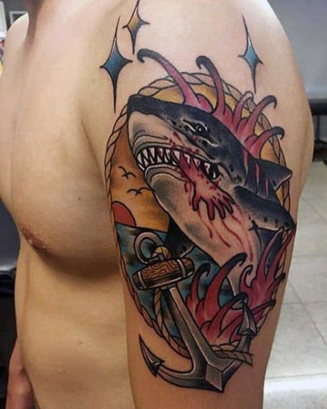 Tatuagem cobrindo o braço e parte do ombro com um tubarão branco saindo da água com um braço dentro de sua mandíbula e uma paisagem ao fundo com o sol e o mar. 