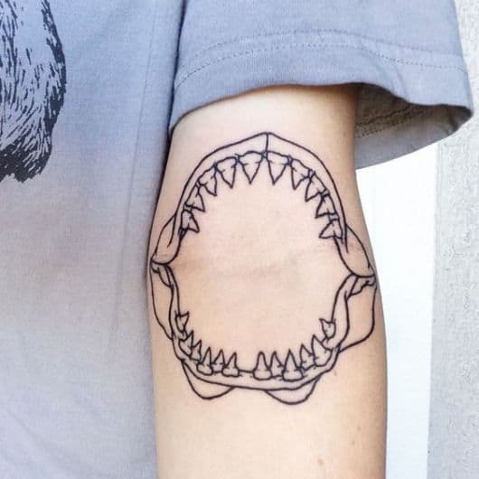 Tatuagem da mandíbula de um tubarão feita na junção entre o braço e o antebraço. 