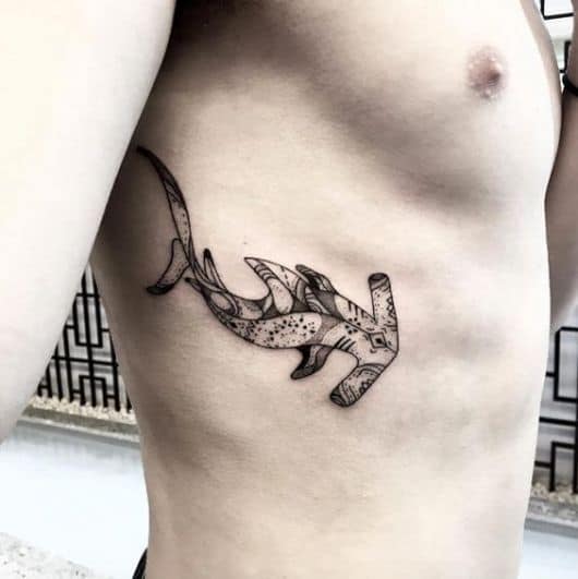 Tatuagem pequena na costela com um tubarão martelo visto de cima pintado como se fosse um quadro. 