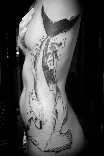 Tatuagem grande na costela que vai das axilas ao quadril de uma mulher. Nela há um tubarão martelo muito bem desenhado. 