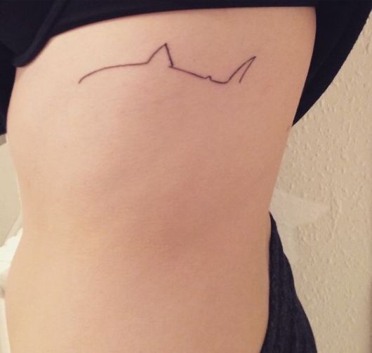 Tatuagem minimalista na costela com a silhueta da parte de cima de um tubarão.