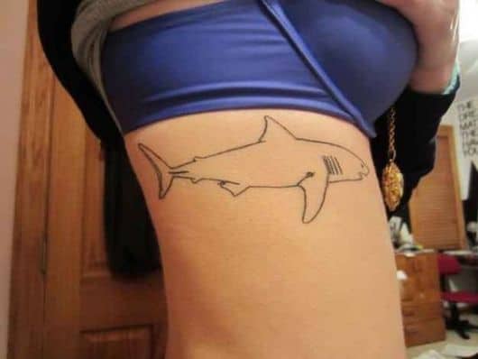 Tatuagem do contorno de um tubarão feita de formas simples mas bem executada na costela de uma mulher. 