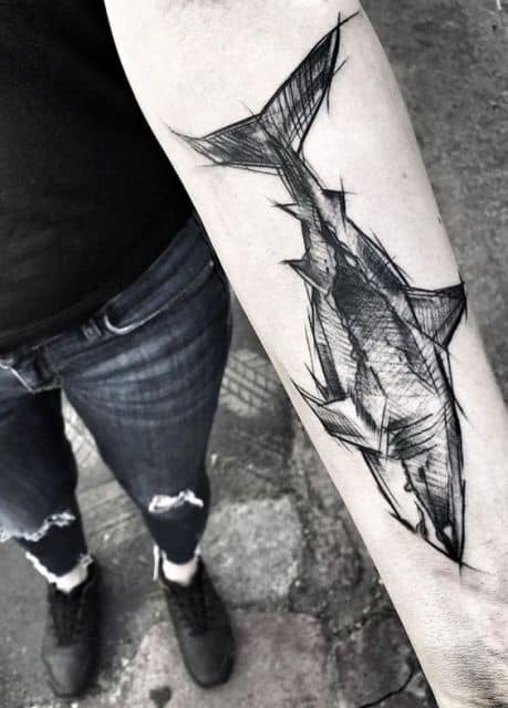 Tatuagem de tubarão no antebraço. Ele é visto de perfil e é feito a partir de rabiscos que simulam um rascunho.