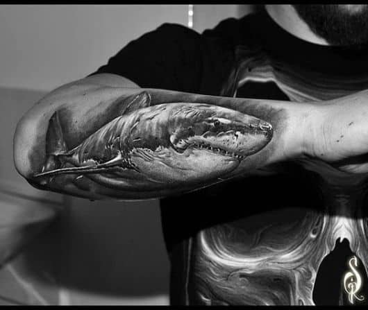 Tatuagem na parte de fora do antebraço. A tattoo é de um tubarão branco com muitas cicatrizes enquanto nada pela água como se estivesse procurando uma presa. 