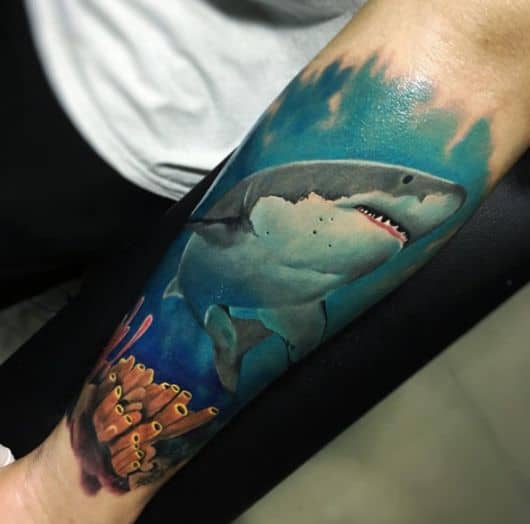 Tatuagem colorida de tubarão no fundo do mar enquanto nada próximo a um conjunto de corais. 