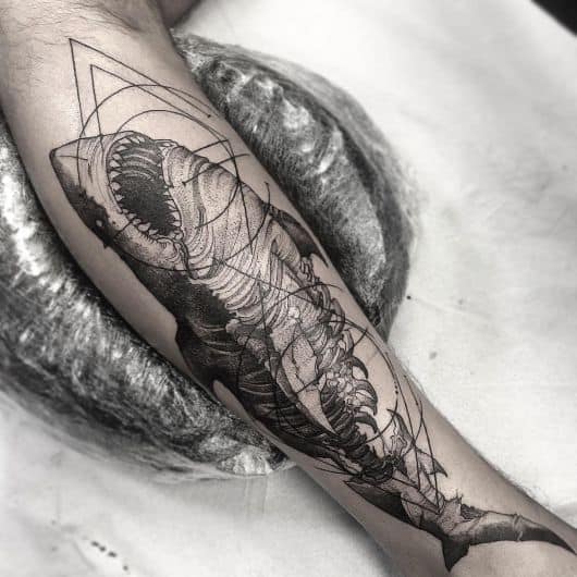 Tatuagem de tubarão com sua barriga aberta e diversas formas geométricas ao seu redor acompanhando sua silhueta. 
