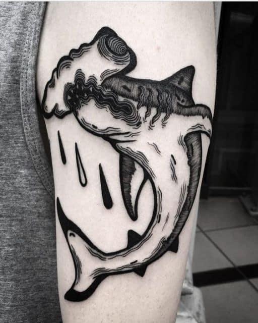 Tatuagem de um tubarão martelo feita com linhas trêmulas que dão a ele um ar psicodélico. 