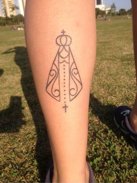 Tatuagem de santinha com cruz na parte traseira da perna.