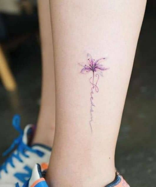 Mulher com tatuagem de flor pequena na lateral da panturrilha na cor roxo claro.