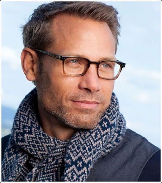 Homem de cachecol olhando para o lado usando um óculos quadrado de grau com as hastes levemente detalhadas. 