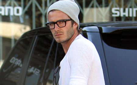 O jogador David Beckham usnado uma camiseta simples branca e um capuz acompanhado de um óculos quadrado de grau com hastes pretas bem definidas. 