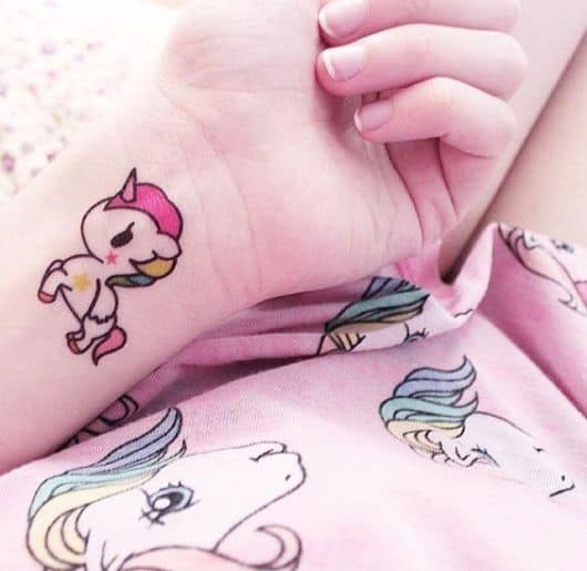 Tatuagem unicórnio pequena com detalhes de cor de rosa.
