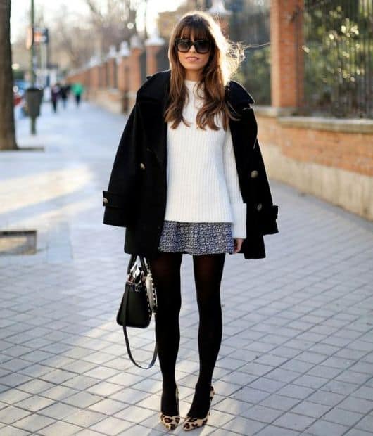 Modelo usa blusa de lã branca, saia curta, meia preta, sapato e bolsa preta.