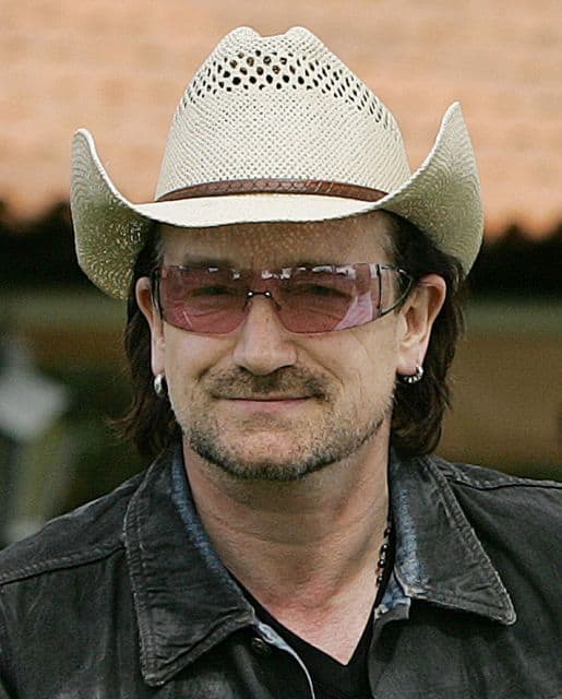Bono Vox sorrindo enquanto usa seu típico chapéu de palha. 