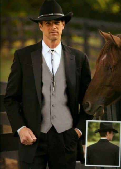 Homem de terno ao lado de um cavalo vestindo trajes sociais e um chapéu country com as coroa baixa. 