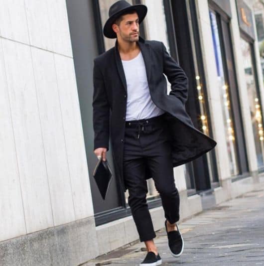Modelo usa calça, casaco, sapato e chapéu fedora preto e camiseta branca.