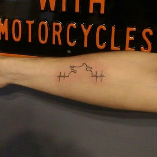 Tatuagem minimalista no antebraço com o desenho de batimentos cardíacos formando a silhueta de uma moto. 