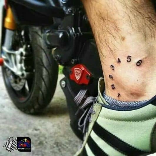 Tatuagem do velocímetro de uma moto no calcanhar de um homem em sua própria moto. 