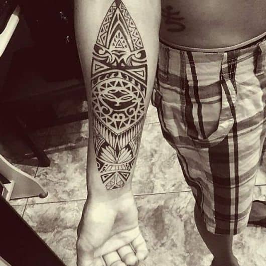 Tatuagem maori no antebraço de um homem em formato de prancha. 