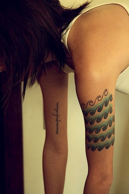 Tatuagem de ondas em diversas camadas feita na parte superior do braço de uma mulher. 