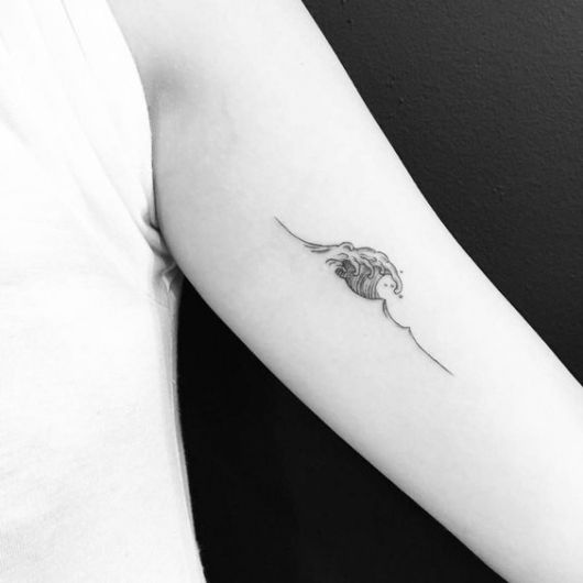 Tatuagem pequena e delicada de uma onda feita na parte interna do braço de uma mulher. 