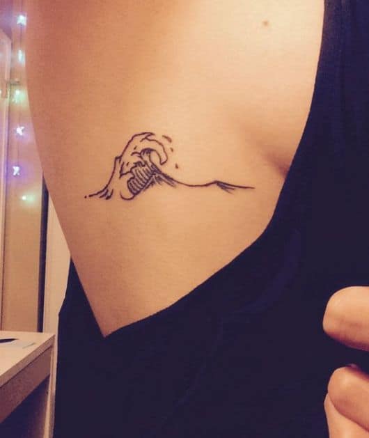 Tatuagem vertical na costela de uma mulher com o desenho de uma onda. 