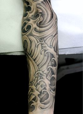 Tatuagem fechando o braço de um homem com o desenho sombreado de ondas em estilo oriental. 