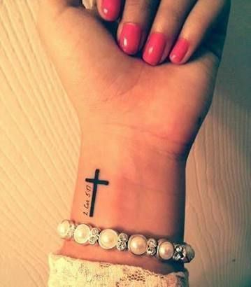 Tatuagem religiosa delicada no pulso de uma mulher com o desenho de uma cruz pintada de preto. 