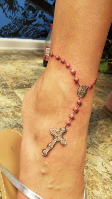Tatuagem de terço que começa no tornozelo de uma mulher e termina com uma cruz no peito do pé. 