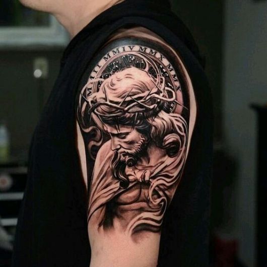 Tatuagem do rosto de Jesus olhando para baixo com uma coroa de espinhos feita na parte superior do braço de um homem. 