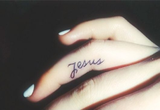 Tatuagem delicada no dedo de uma mulher escrito "Jesus"