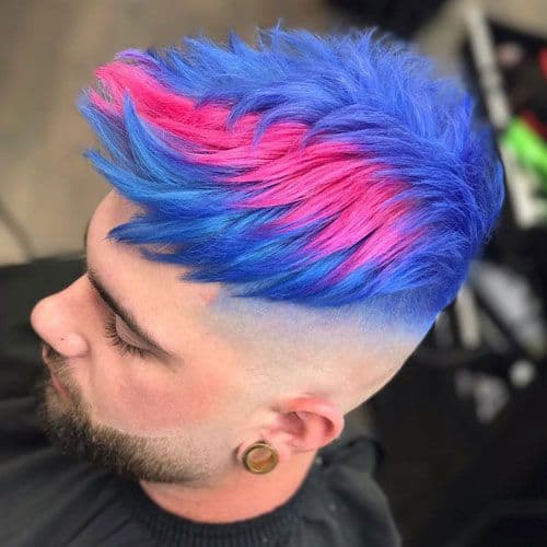 Homem no cabeleiro com a lateral do cabelo completamente raspada e o topo com um pequeno topete todo pintado de azul com uma pequena listra rosa. 