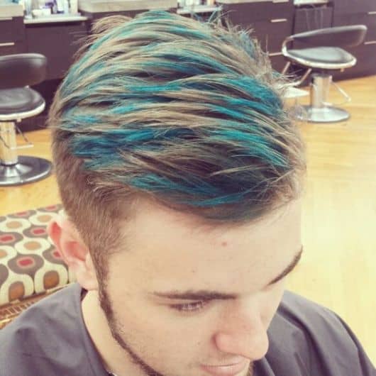 Homem no cabeleireiro com seu cabelo recém-cortado e o topo pintado com luzes azuis.  