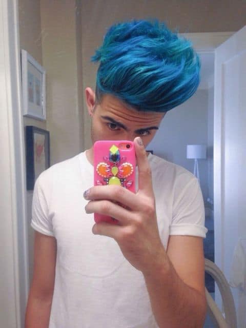 Homem tirando um selfie no banheiro. Ele tem um cabelo longo jogado para o lado todo pintado de azul. 