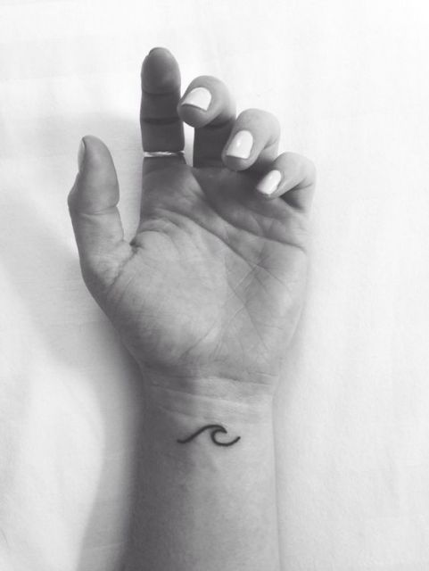Tatuagem pequena e delicada no pulso de uma mulher com o desenho de uma onda pequena formada por uma linha. 