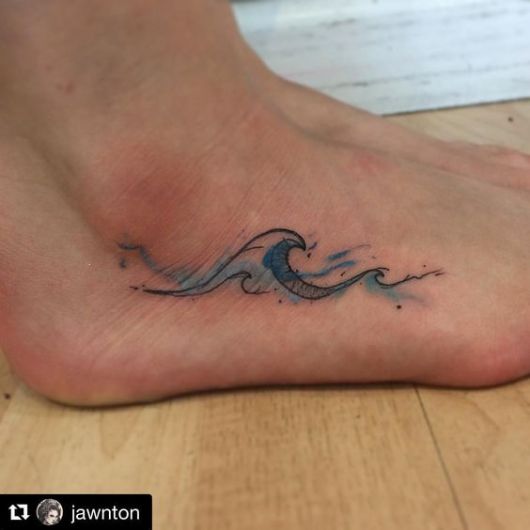 Tatuagem na lateral do pé com o desenho de ondas no mar pintadas levemente com aquarela azul. 