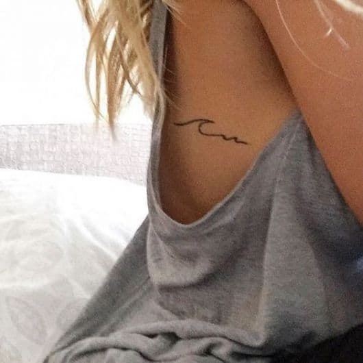 Mulher de regata cavada com a tatuagem minimalista de uma onda na costela. 