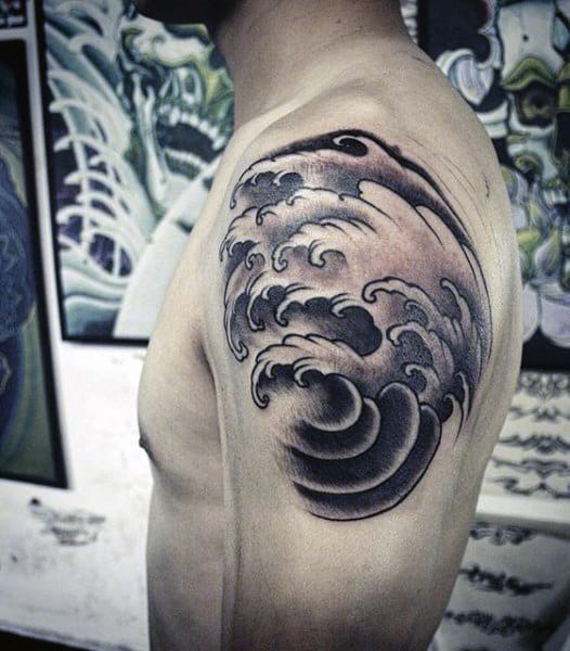 Tatuagem cobrindo o ombro de um homem com o desenho de ondas agitadas em estilo oriental. 