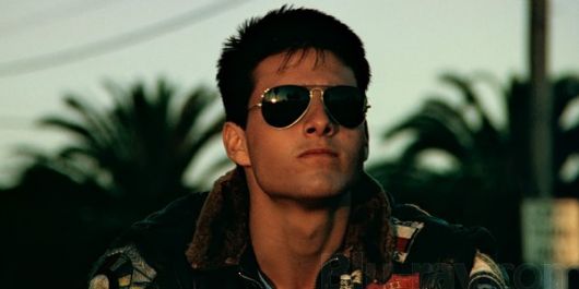 Tom Cruise no filme Top Gun olhando para o horizonte com um óculos aviador masculino de sol no rosto. 