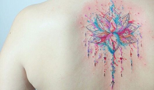 tatuagem flor de lótus nas cores azul, vermelho e rosa, nas costas.