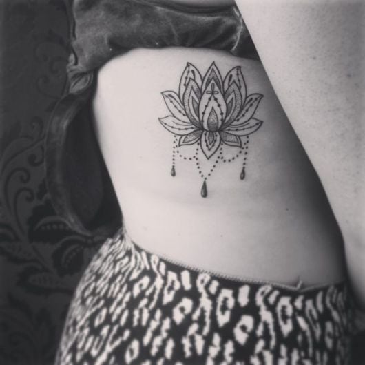 tatuagem preta e branca de flor de lótus na costela, tamanho grande.