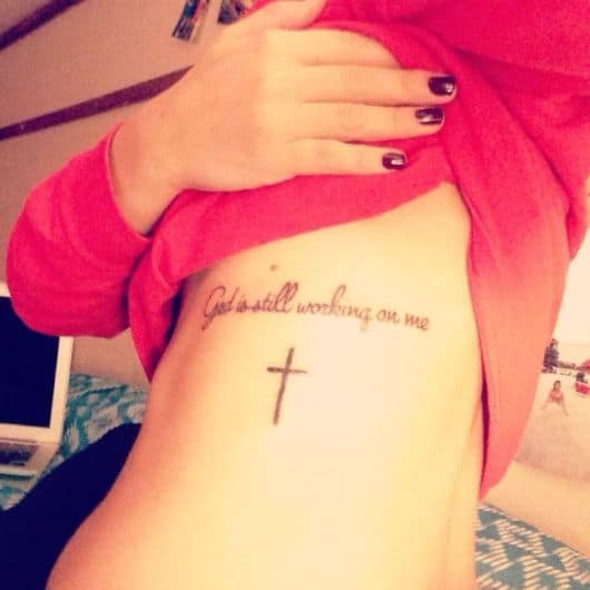 Tatuagem de cruz na costela com frase religiosa