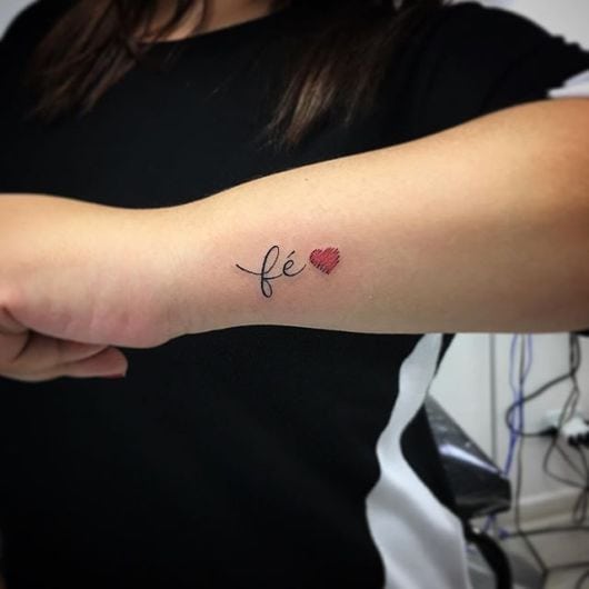 tatuagem escrita no pulso com a palavra fé e um coração vermelho.