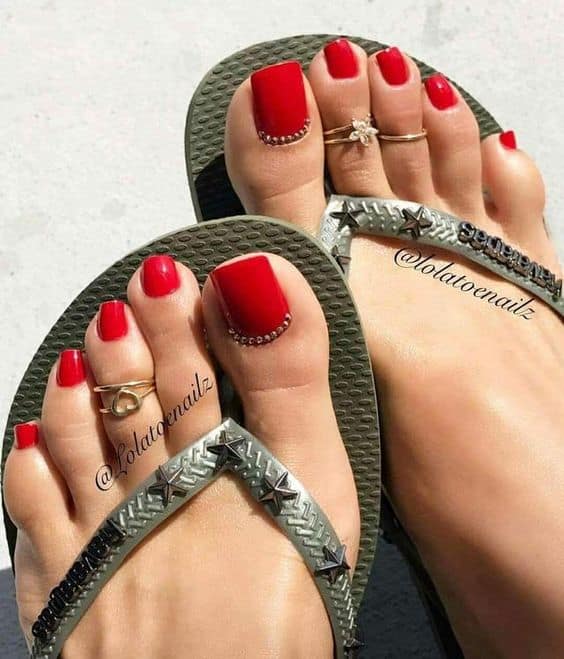 unhas do pé com esmalte vermelho e joias