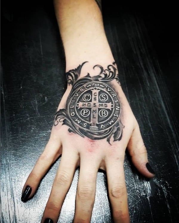 38 tatuagem feminina medalha de São Bento na mão @jozimarbergertattoo
