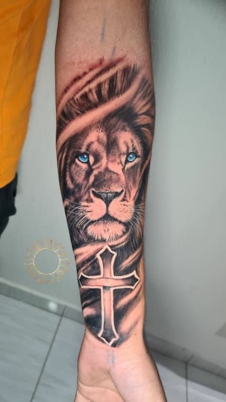 Tatuagem leão com cruz no braço masculino